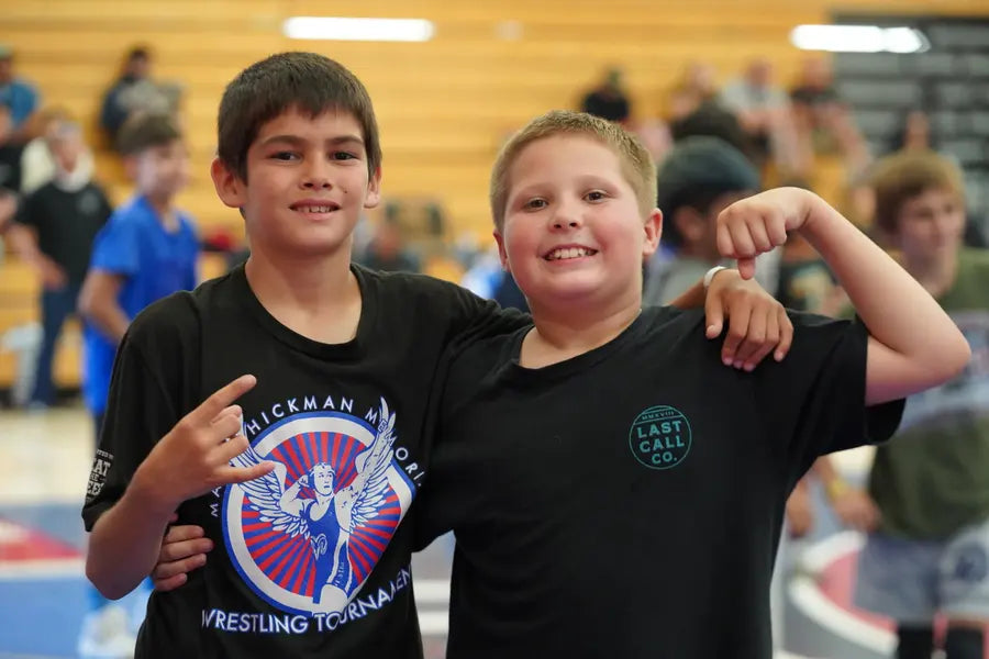 Two young teammates arm in arm and smiling at a wrestling tournament