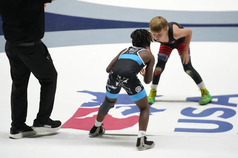 Two youth wrestlers squaring off at the center of a USA Wrestling tournament mat